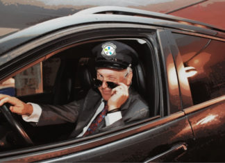 Dr Leduc déguisé en chauffeur de limousine, le logo d'Agrément sur sa casquette. Il a baissé ses lunettes de soleil et fait un clin d'oeil.