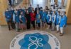 Groupe de personnes portant chacun une veste bleue, entourant un collant géant sur le sol à l'effigie d'un papillon