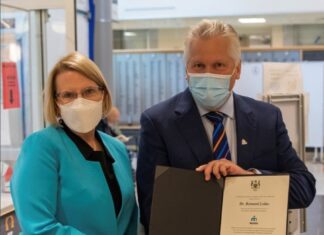 Une femme et un homme masqués sont côte à cote; l'homme tient un document officiel entre ses mains
