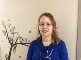 Cathy, vêtue d'un uniforme bleu, et portant un stéthoscope sur l'épaule, souriante dans un corridor de l'hôpital