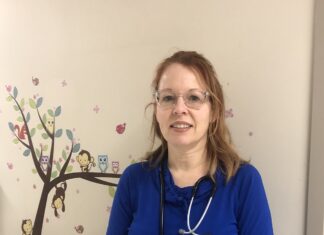 Cathy, vêtue d'un uniforme bleu, et portant un stéthoscope sur l'épaule, souriante dans un corridor de l'hôpital