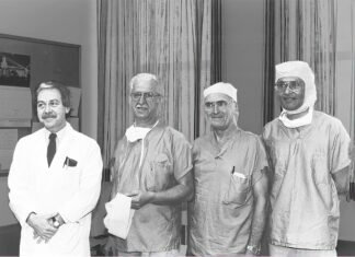 Photo d'archive en noir et blanc, quatre chirurgiens vêtus pour entrer à la salle d'opération