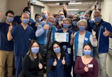 Groupe de membres du personnel hospitalier dans un corridor. Ils sont souriants malgré le port du masque et font tous le signe du pouce en l'air. la personne au milieu de l'image tient un certificat dans ses mains