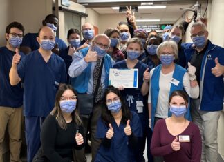 Groupe de membres du personnel hospitalier dans un corridor. Ils sont souriants malgré le port du masque et font tous le signe du pouce en l'air. la personne au milieu de l'image tient un certificat dans ses mains