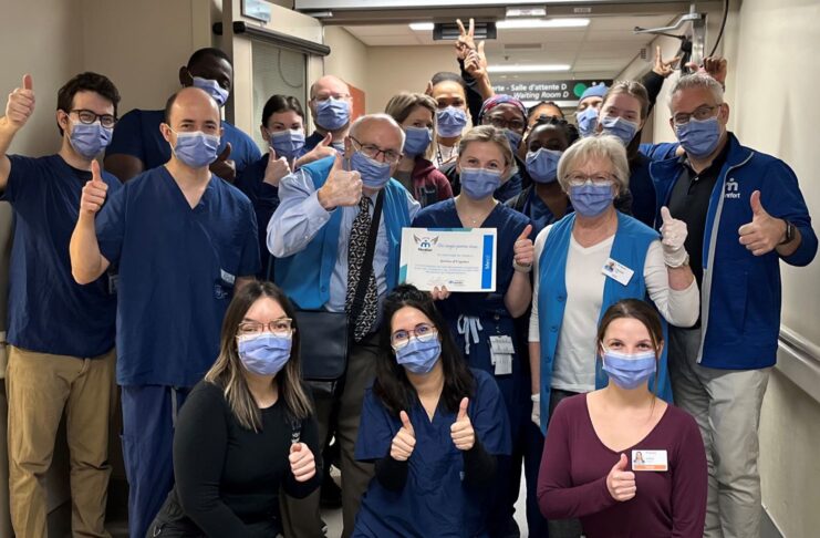 Groupe de membres du personnel hospitalier dans un corridor. Ils sont souriants malgré le port du masque et font tous le signe du pouce en l'air. la personne au milieu de l'image tient un certificat dans ses mains
