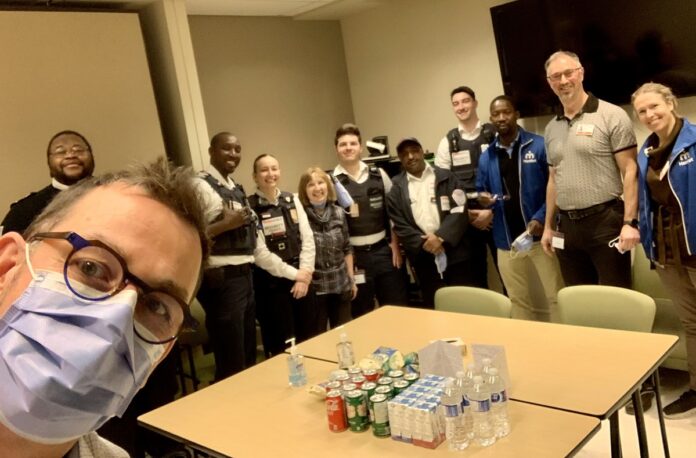 Le gestionnaire du programme de santé mentale fait un selfie dans une salle de réunion. Derrière lui, un groupe de membres de l'équipe au programme de santé mentale, accompagnés de membres de l'équipe de Sécurité. Des cannettes de boissons gazeuses et de jus sont sur une table.