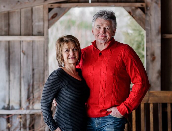 Photo d'une femme et d'un homme cinquantenaires souriants, dans une grange