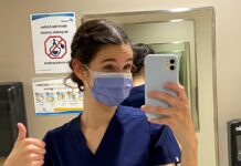 Jeune femme masquée et portant des "scrubs" qui prend un selfie dans une salle de bain de Montfort avant son premier quart de travail