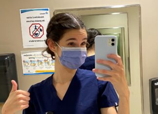 Jeune femme masquée et portant des "scrubs" qui prend un selfie dans une salle de bain de Montfort avant son premier quart de travail