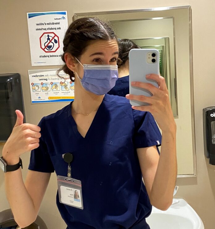 Nina à Montfort Jeune femme masquée et portant des "scrubs" qui prend un selfie dans une salle de bain de Montfort avant son premier quart de travail