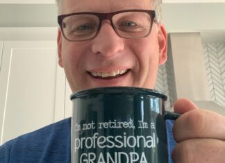 Philippe Marleau souriant, tenant bien en évidence une tasse où il est écrit (en anglais) qu'il n'est pas retraité mais un grand-père à plein temps.